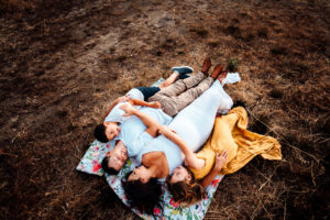 Family Photographer, a young family lays on a picnic blanket outside lying beside each other