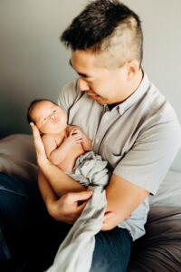 Newborn Photographer, a father holds his new baby child in his arms at home