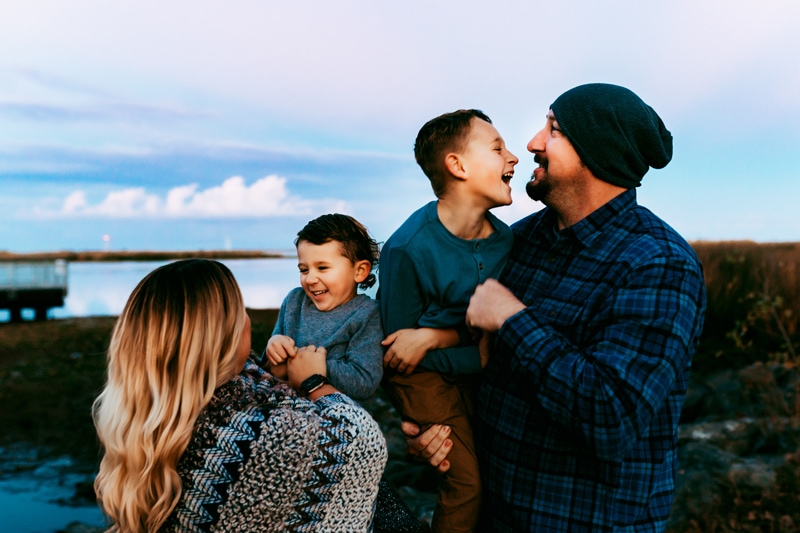 Family Photographer, a mother and father hold their young giggling boys at sunset