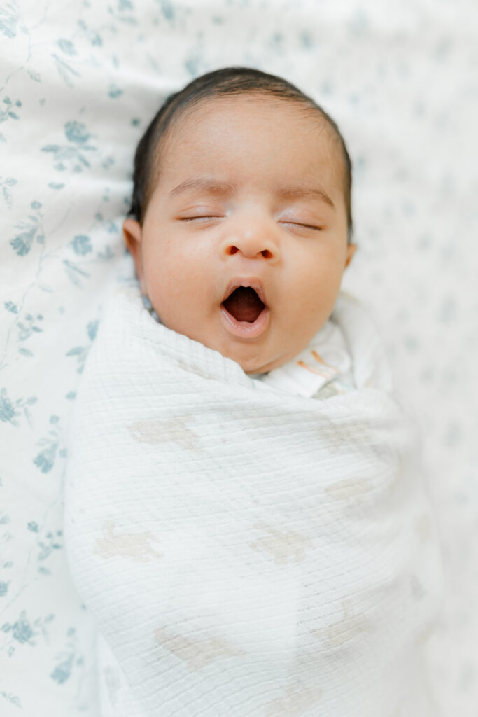 A newborn baby lays in a floral onesie on a bed with eyes open thanks to a Bay Area Labor And Delivery Center