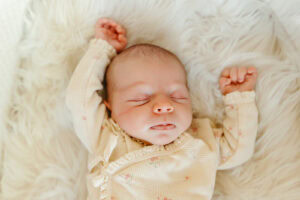 A newborn girl sleeping on a white fur rug.