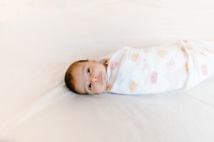 A baby girl in a white wrap laying on a bed.