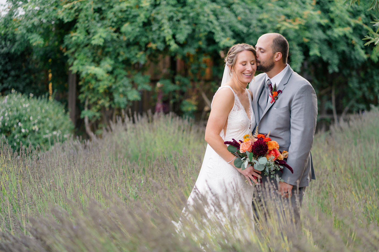 Newlyweds snuggle and smile while exploring a lavender garden at sunset
