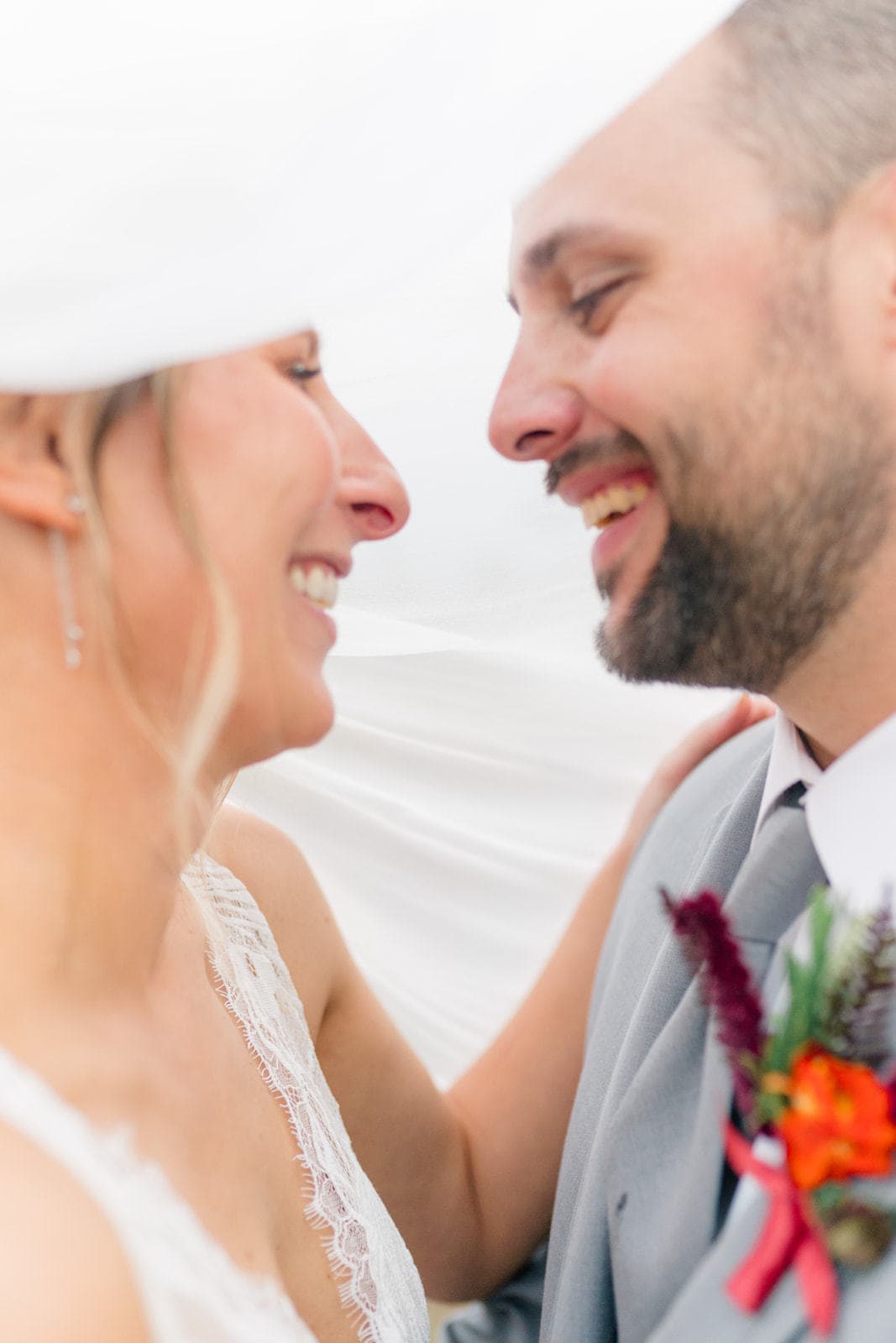A bride and groom laugh while leaning in for a kiss under the veil