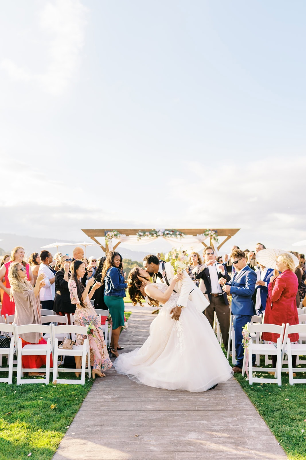Newlyweds kiss in the aisle to end their outdoor ceremony as guests applaud at one of the wedding venues in Brentwood, CA