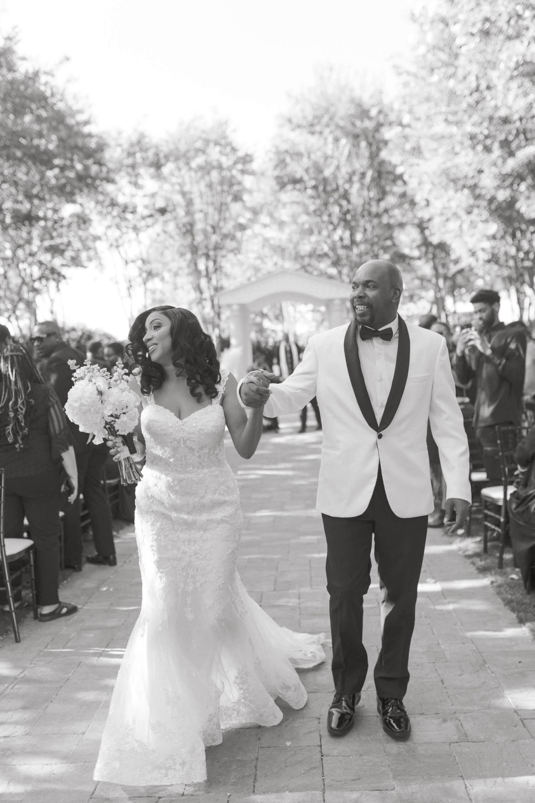 Black and White photo of wedding couple after just saying i do at the palm event center smiling at the audience while walking