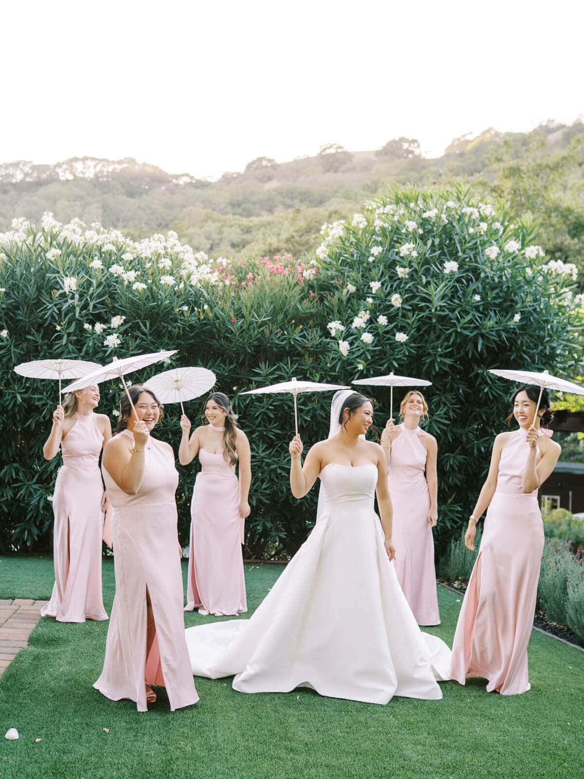 Bride and bridesmaids in blush pink dresses pose with parasols during an Elliston Vineyards wedding in Sunol, California.