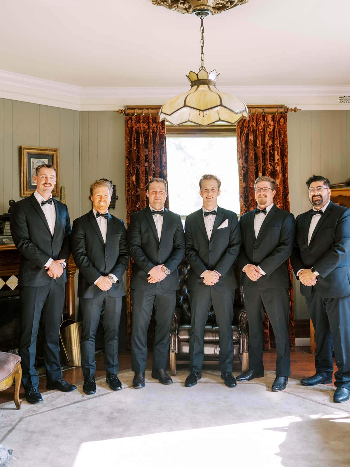 Groom and groomsmen in classic black tuxedos pose together while getting ready for an Elliston Vineyards wedding.