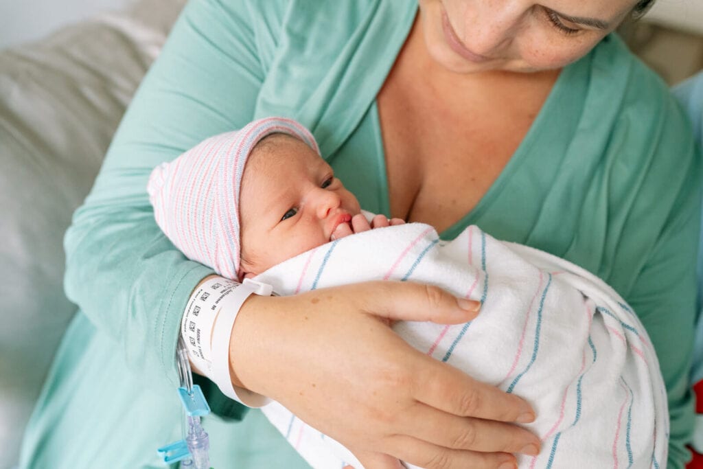 Mom snuggling newborn baby in hospital bed during a Fresh 48 photography session
